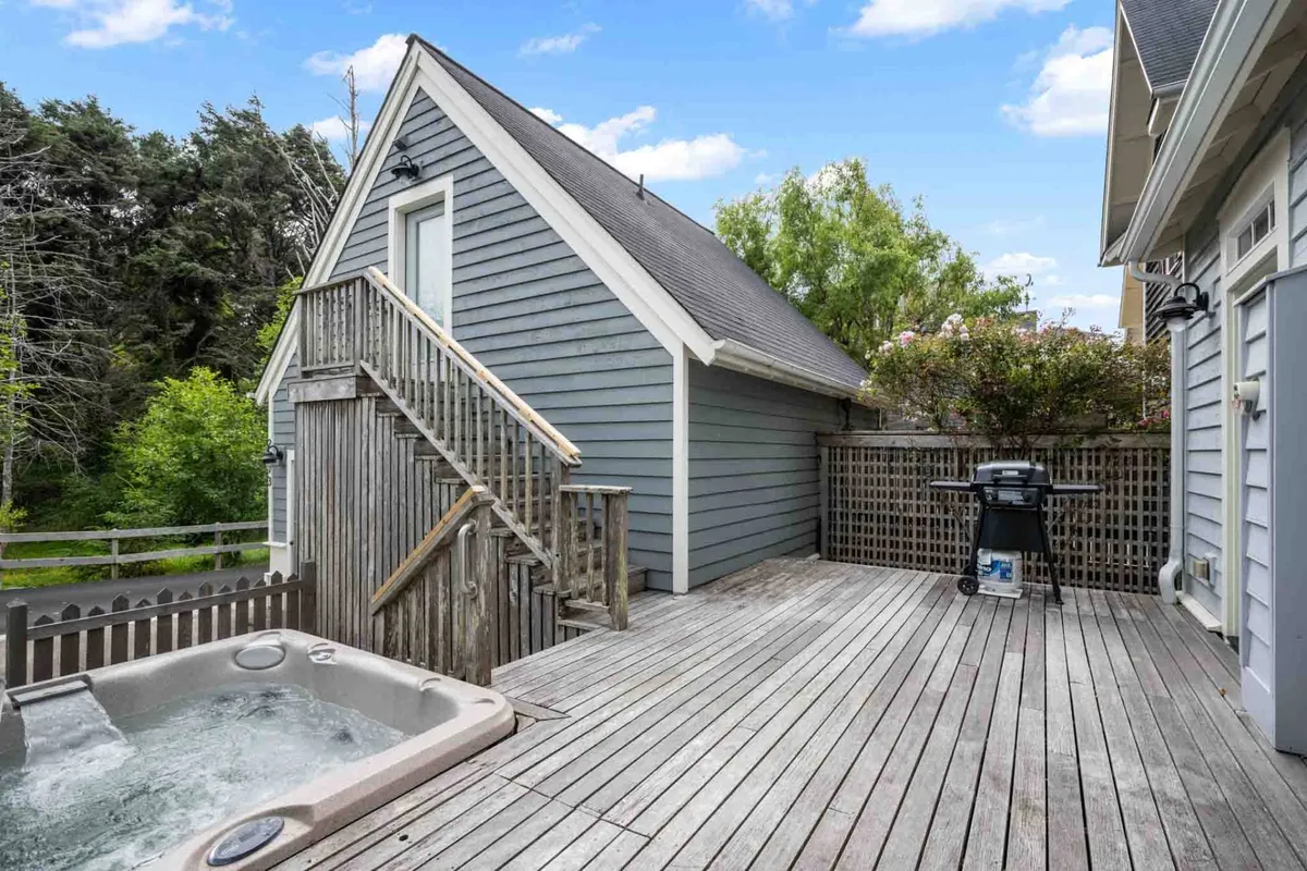 This image features a deck with a hot tub, grill, and comfortable seating, set against a scenic backdrop. The stairs lead to an upper level, and the area is perfect for barbecues, al fresco dining, and unwinding at the end of the day.
