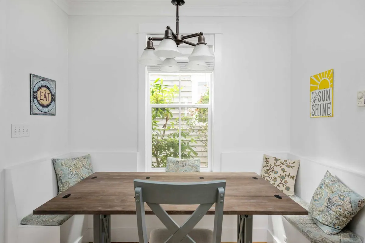 An elegant dining area featuring a beautifully set dining table beneath a chandelier, accented by wall art and a window offering natural light and views. The setting is perfect for intimate meals or lively gatherings.