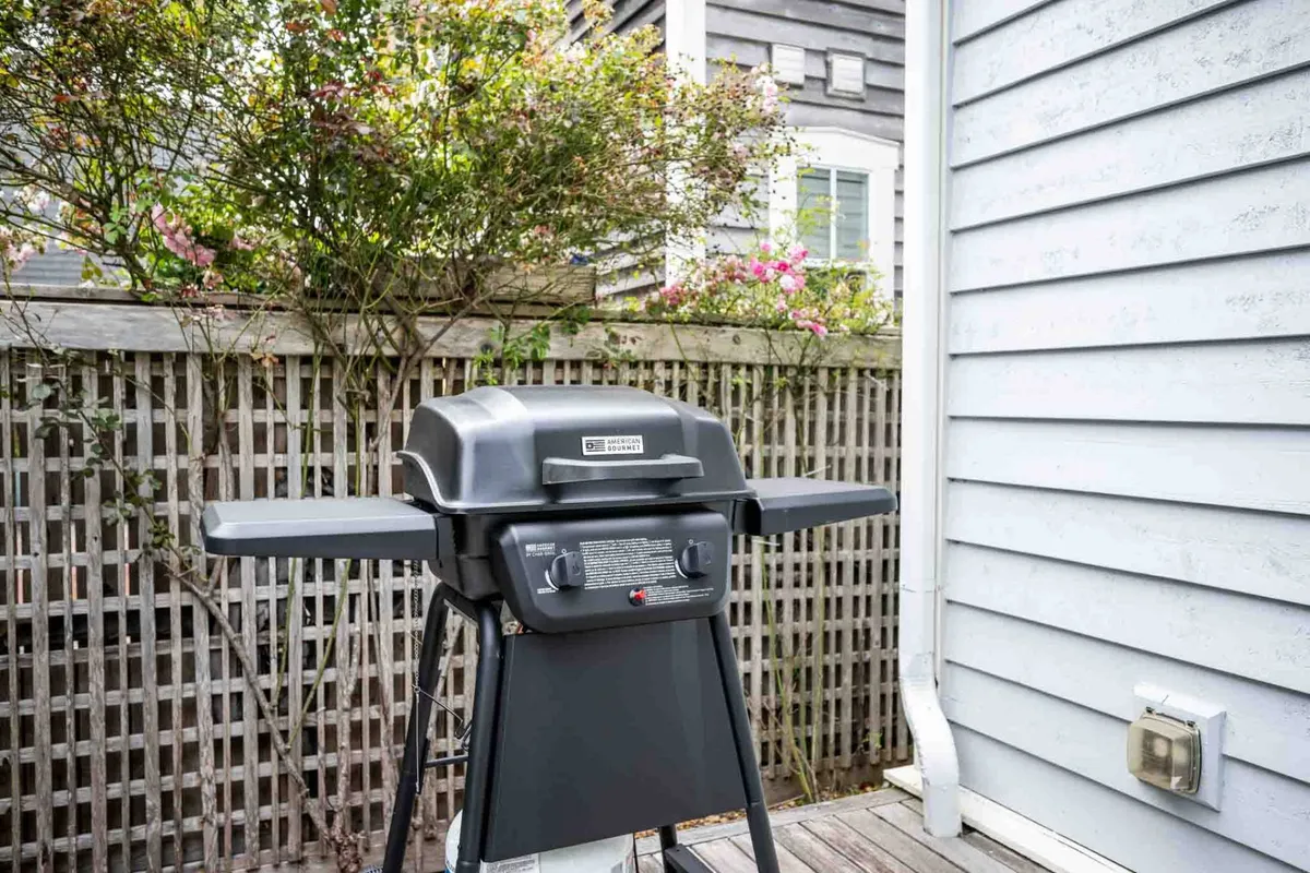 This exterior image features a grill set against lush greenery, enclosed by a wooden fence. The scene suggests a private and tranquil outdoor space, perfect for relaxing evenings, outdoor dining, and casual family gatherings.