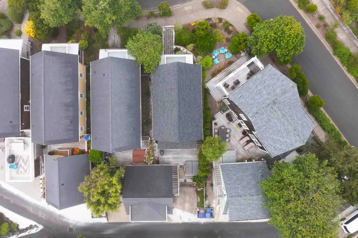 A welcoming exterior view featuring several cottage rooftops nestled among green foliage, with an outdoor seating area in the foreground. People are seen participating in outdoor gatherings and neighborhood walks, reinforcing the sense of a lively community.