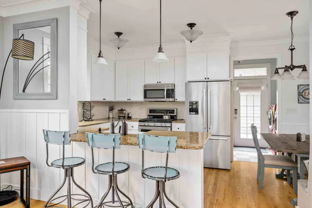 A welcoming kitchen scene with granite countertops, bar stools tucked under a kitchen island, and stainless steel appliances gleaming in the background. The arrangement invites conversation and casual dining, with hardwood floors visible.