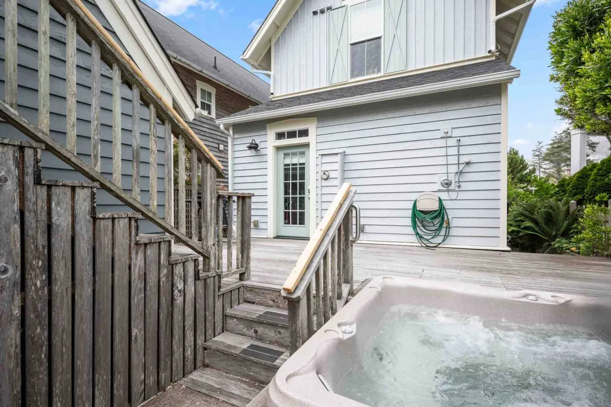 This image focuses on the private hot tub situated just outside the house, adjacent to a staircase and exterior door. The area is surrounded by greenery, enhancing the feeling of privacy and tranquility; the lighting suggests either a peaceful morning or an inviting twilight moment.