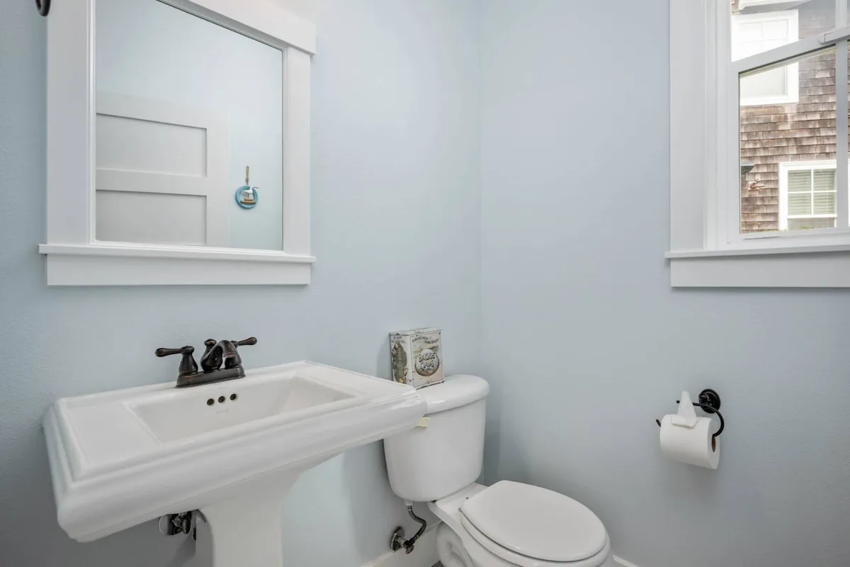 A compact half bath with a white sink, mirror, toilet, and light blue walls, offering a calm and functional spot for freshening up. The space feels crisp and accessible.