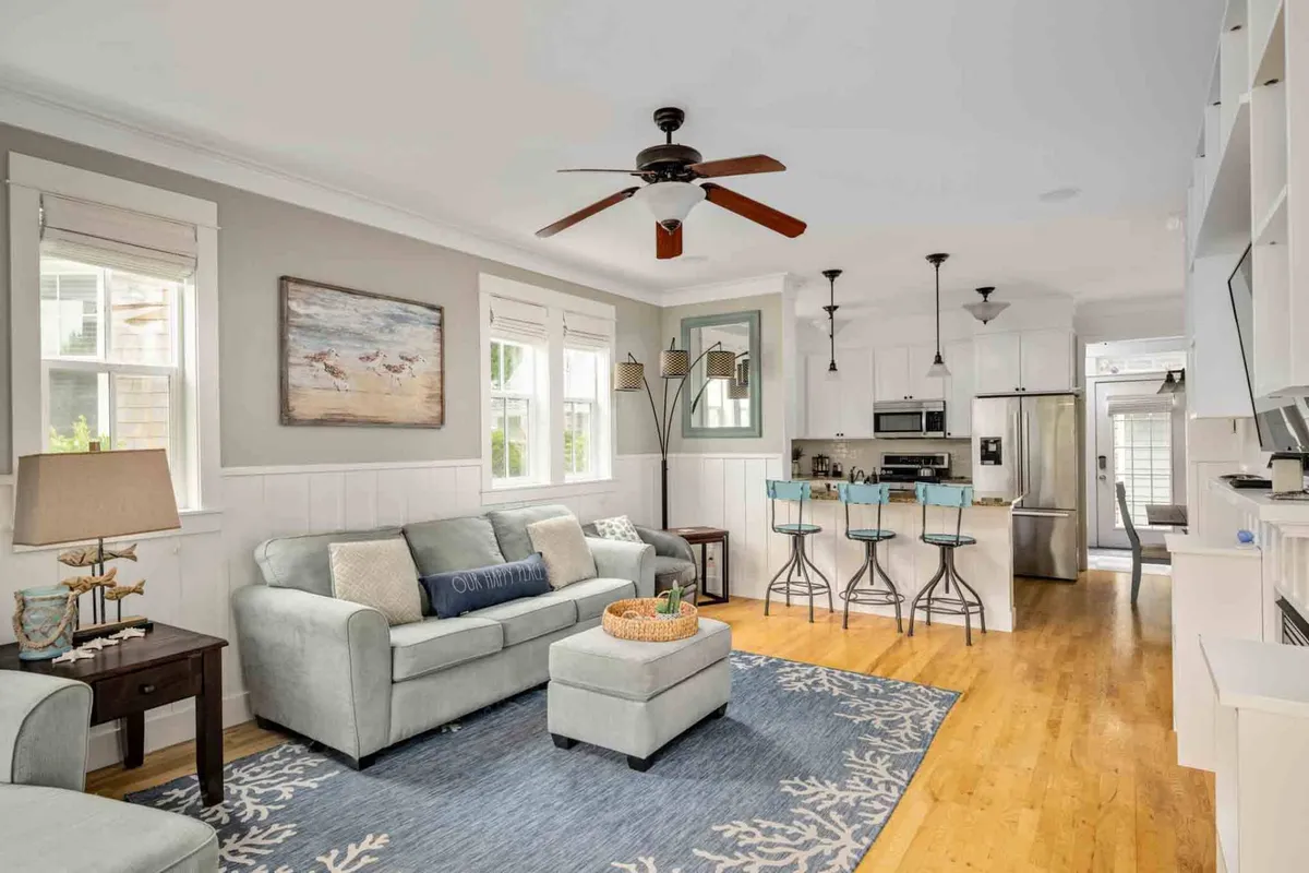 A spacious, open-concept area showcasing a comfortable sofa, striking artwork on the wall, a prominent kitchen island, warm flooring, and elegant lighting fixtures. The living and kitchen spaces are visibly connected, emphasizing the unified atmosphere described in the section.